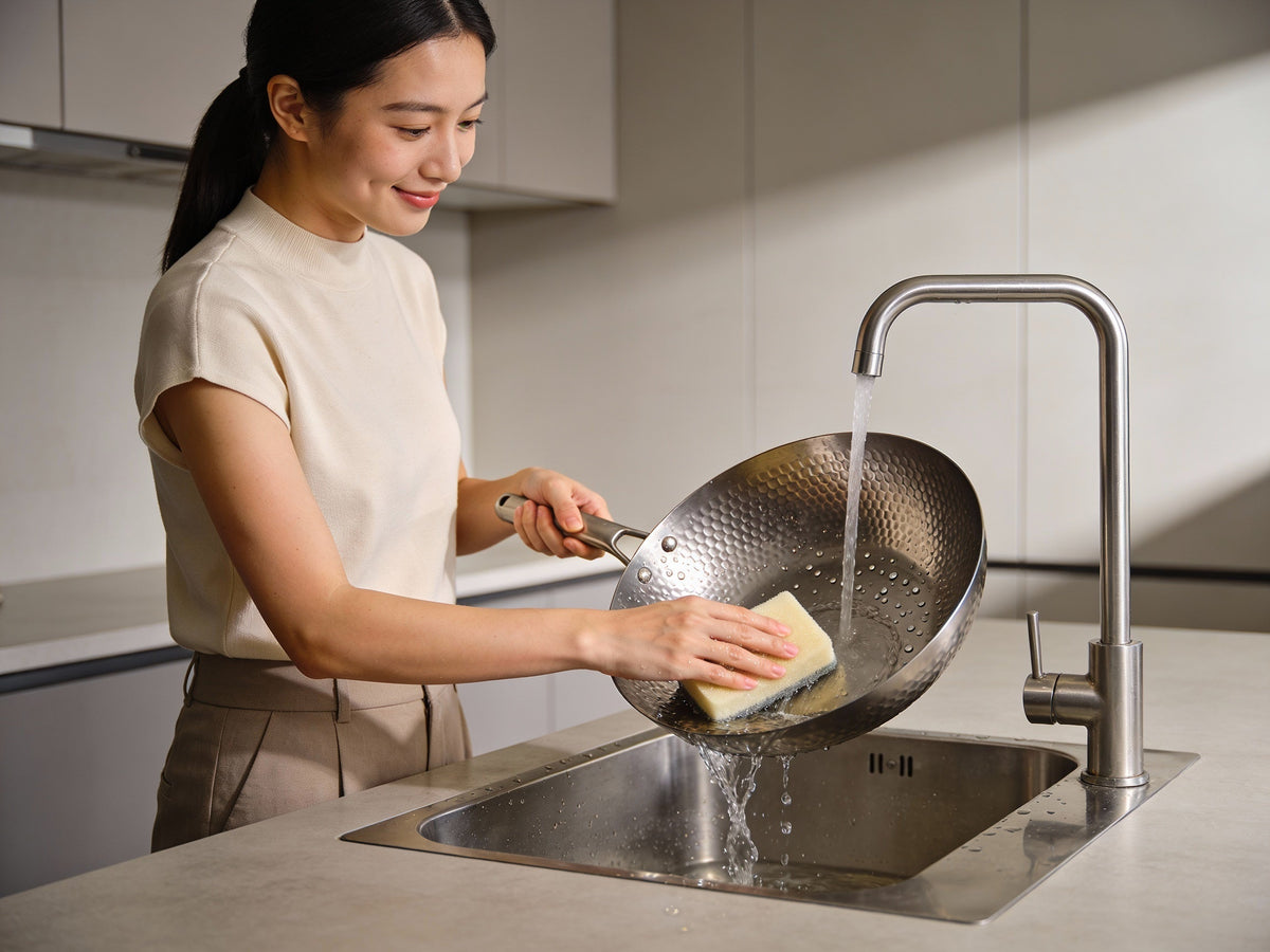Woman washing a hammered titanium pan with a sponge at the sink, how to clean titanium cookware