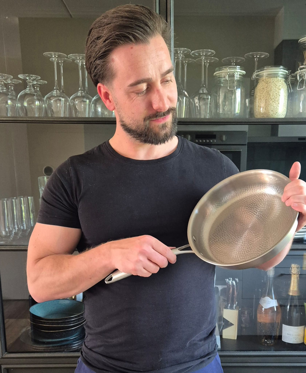 Man in a kitchen admiring a Siraat titanium pan, cook strong, cook smart with titanium cookware